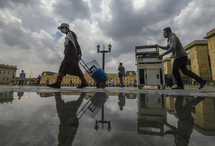 Vendedores ambulantes con tapabocas caminan en la plaza Bolívar, en Bogotá.